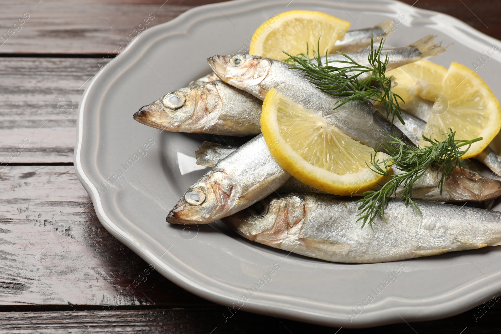 Photo of Fresh raw sprats, dill and cut lemon on wooden table, closeup