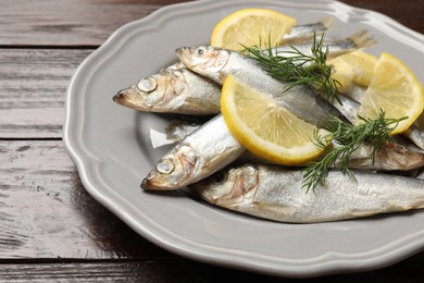 Fresh raw sprats, dill and cut lemon on wooden table, closeup