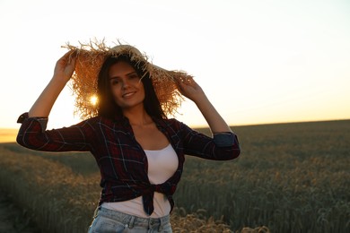 Photo of Beautiful young woman in straw hat among ripe wheat field on sunny day, space for text