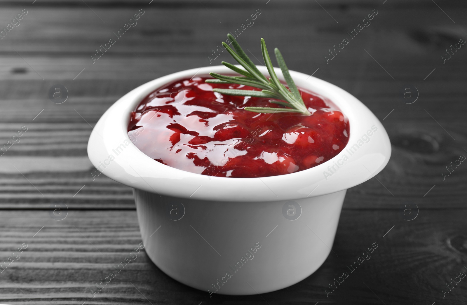 Photo of Fresh cranberry sauce in bowl and rosemary on black wooden table, closeup