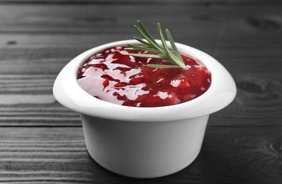 Photo of Fresh cranberry sauce in bowl and rosemary on black wooden table, closeup