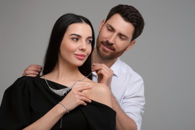 Photo of Man putting elegant necklace on beautiful woman against grey background