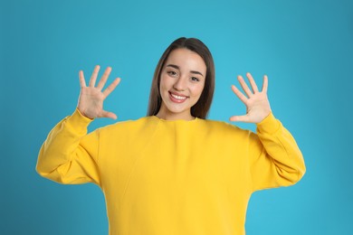 Photo of Woman showing number ten with her hands on light blue background