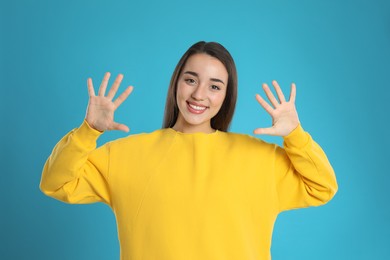 Woman showing number ten with her hands on light blue background