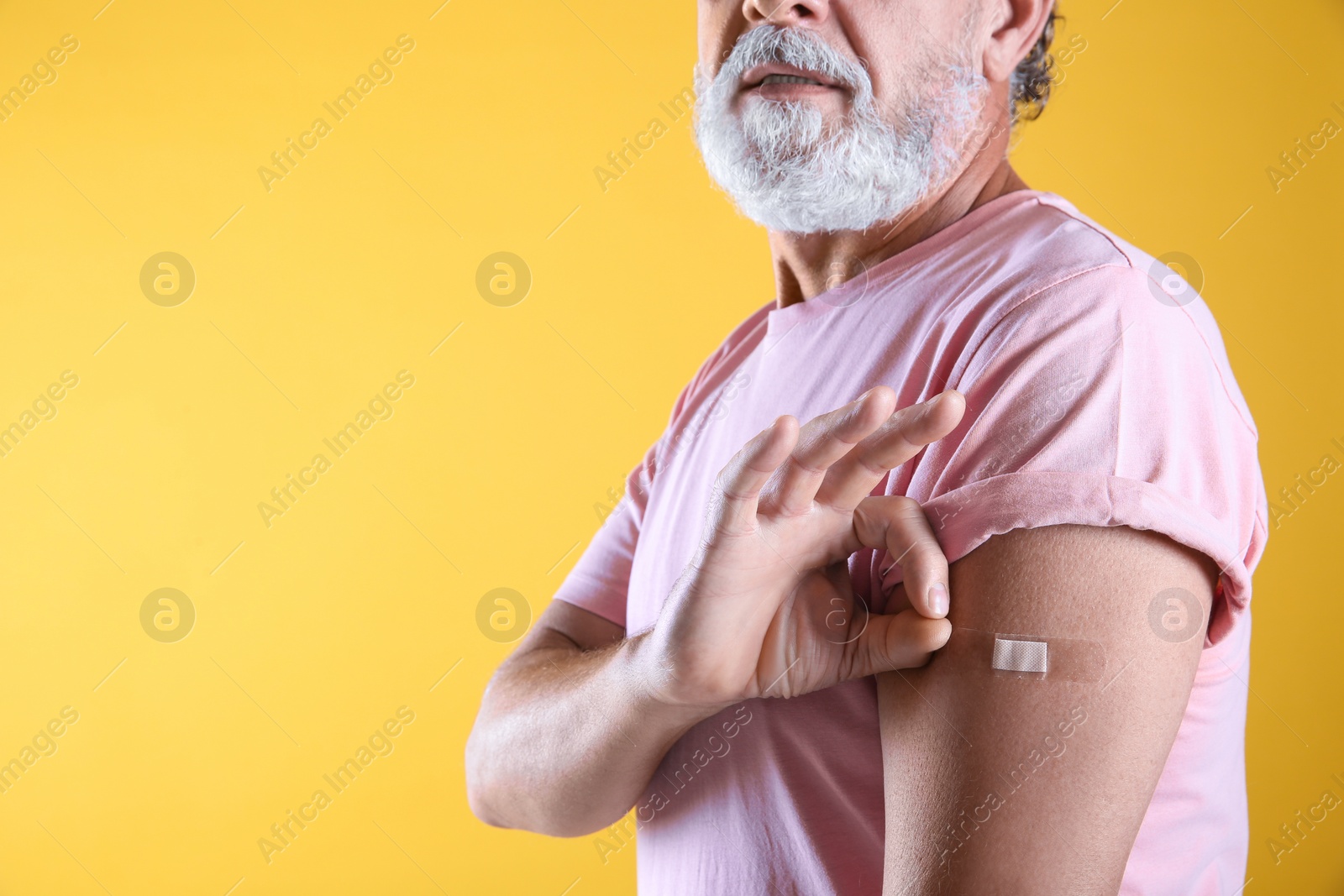 Photo of Senior man showing arm with bandage after vaccination on yellow background, closeup