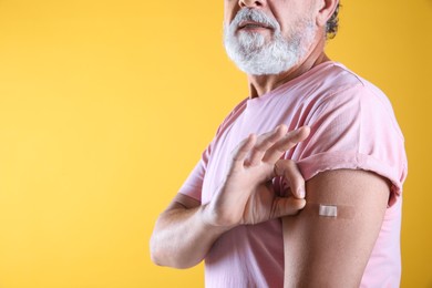 Photo of Senior man showing arm with bandage after vaccination on yellow background, closeup