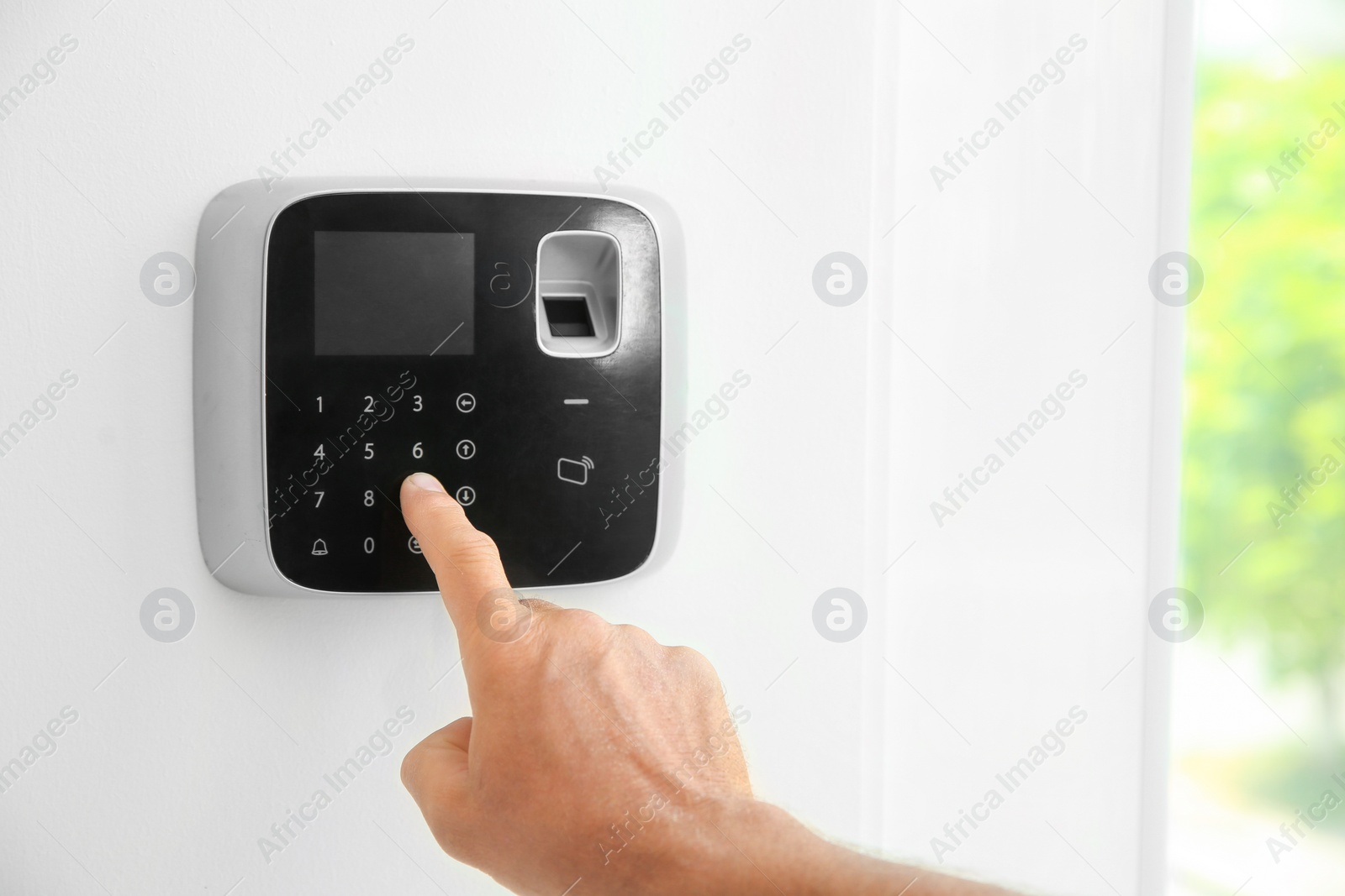 Photo of Mature man entering code on alarm system keypad indoors