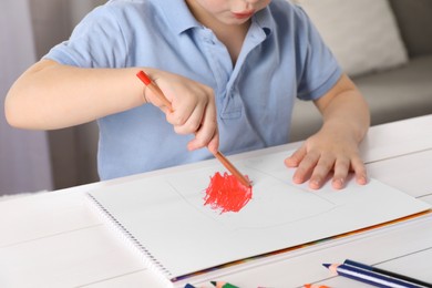 Photo of Little boy drawing with pencil at white wooden table, closeup. Child`s art
