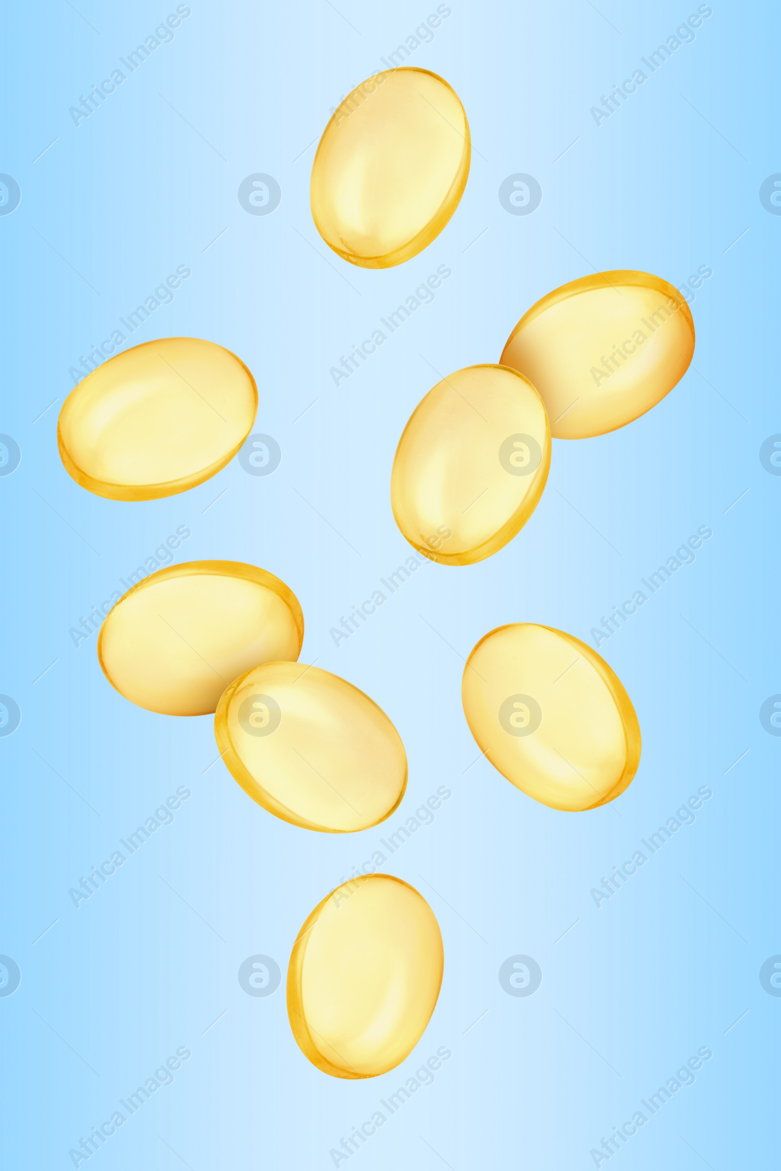 Image of Vitamin. Softgel capsules falling on light blue gradient background