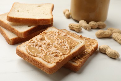 Photo of Delicious toasts with peanut butter and nuts on white table, closeup