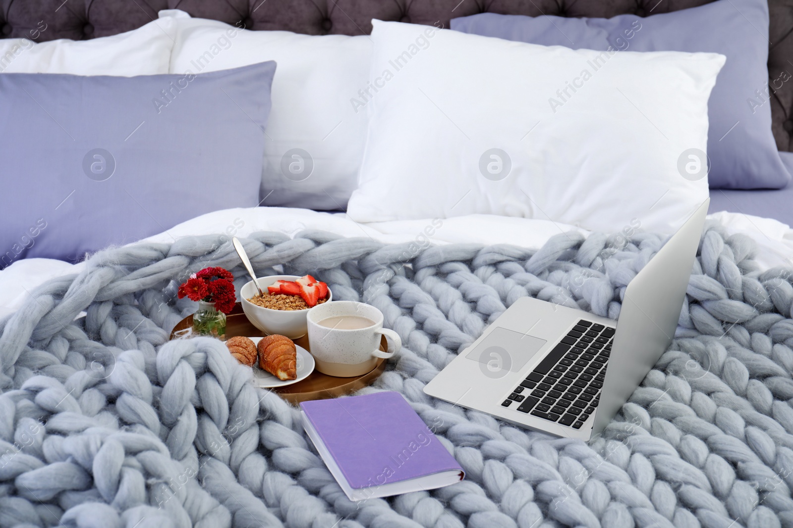 Photo of Laptop, tray with breakfast and notebook on bed. Interior element