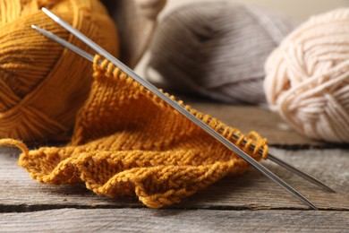 Photo of Soft orange knitting, yarns and metal needles on wooden table, closeup