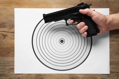 Photo of Man with handgun and shooting target on wooden table, top view
