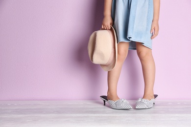 Photo of Little girl in oversized shoes near color wall with space for text, closeup on legs