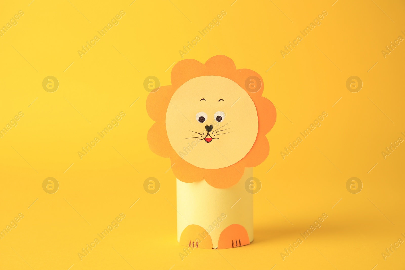 Photo of Toy lion made from toilet paper hub on yellow background. Children's handmade ideas