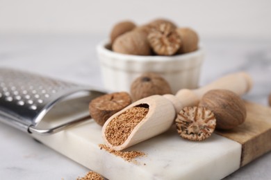 Photo of Scoop with grated nutmeg, seeds and grater on white table