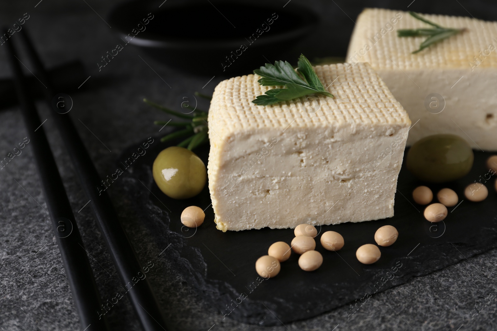 Photo of Pieces of delicious tofu with herbs, olives and soy on grey table, closeup