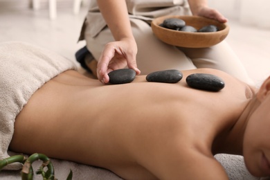 Beautiful young woman getting hot stone massage in spa salon