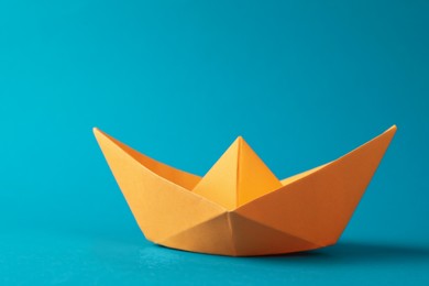 Photo of Handmade orange paper boat on light blue background.  Origami art