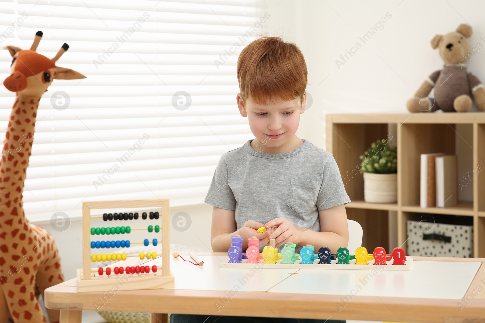 Photo of Little boy playing with Educational game Fishing for Numbers at desk in room. Learning mathematics with fun