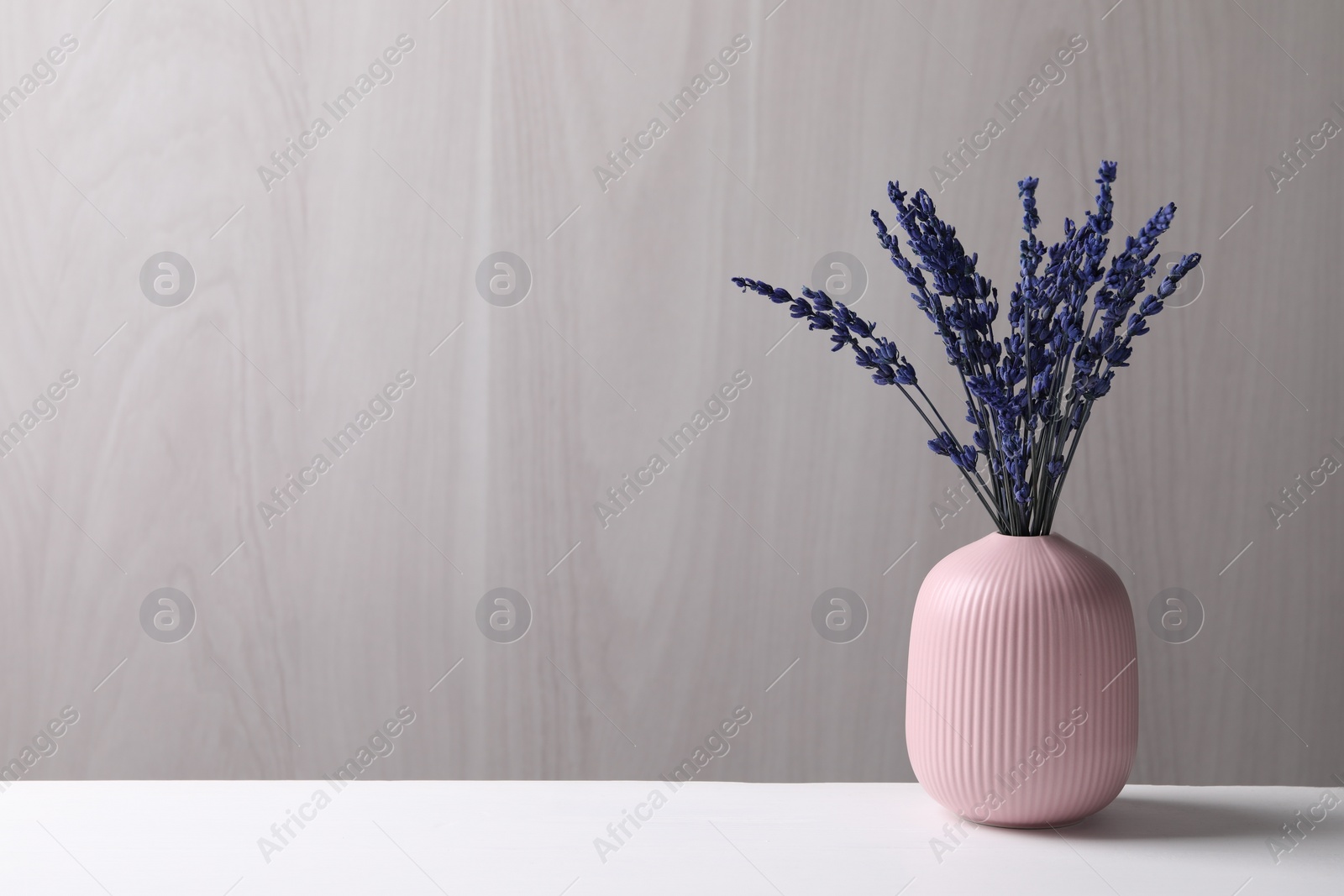 Photo of Bouquet of beautiful preserved lavender flowers on white table near grey wooden wall, space for text