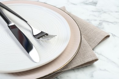 Photo of Clean plates, cutlery and napkin on white table, closeup