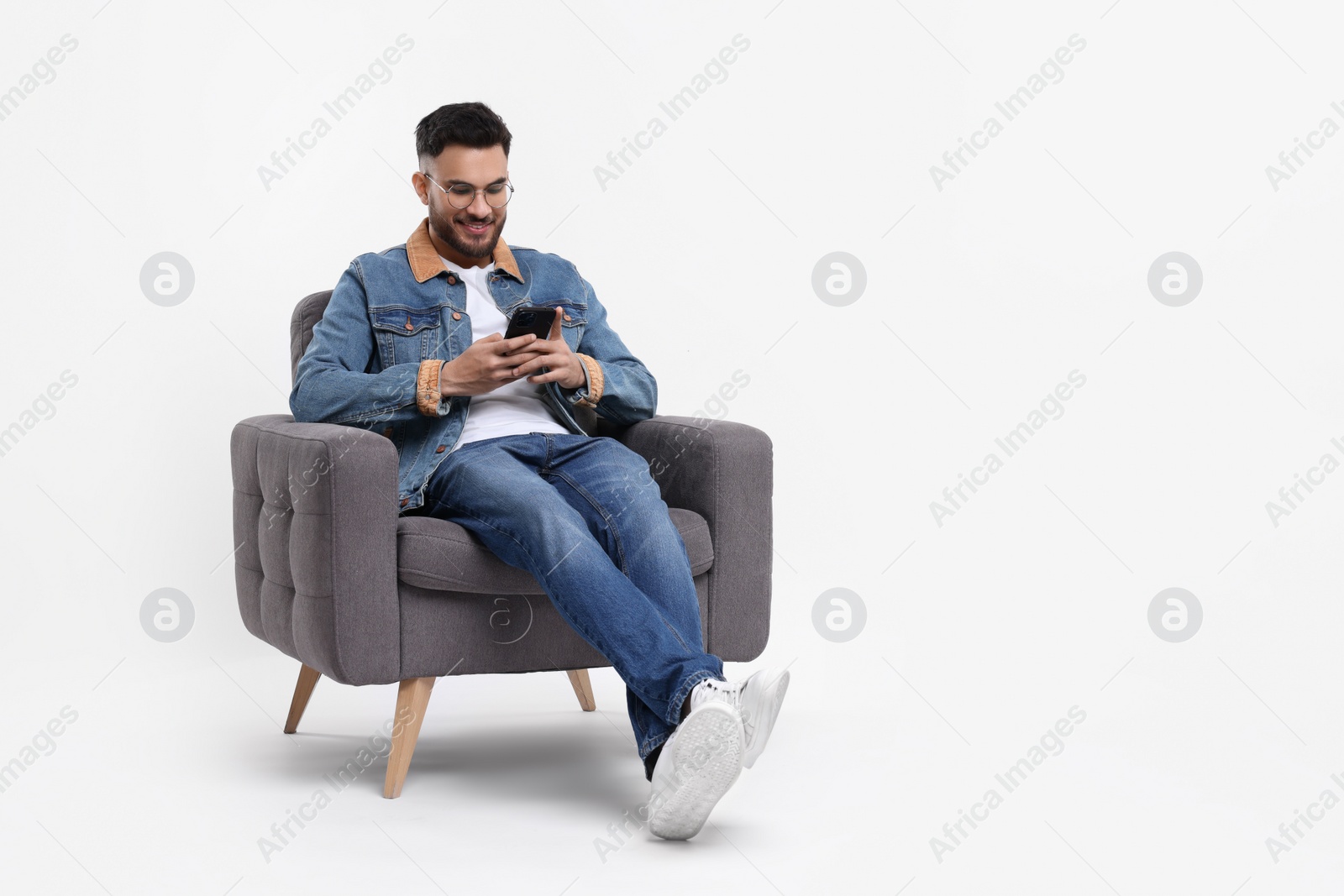 Photo of Happy man using smartphone in armchair on white background, space for text