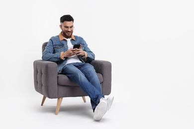 Photo of Happy man using smartphone in armchair on white background, space for text