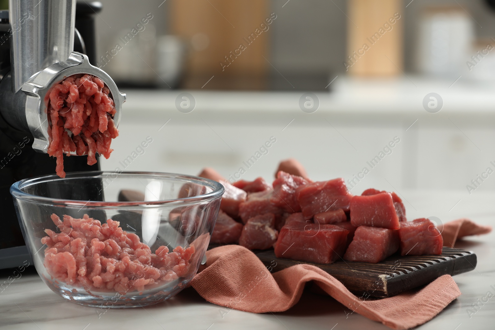 Photo of Electric meat grinder with beef mince on white table against blurred background, closeup. Space for text