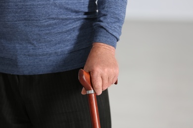 Photo of Elderly man with walking cane on blurred background, closeup of hand. Space for text