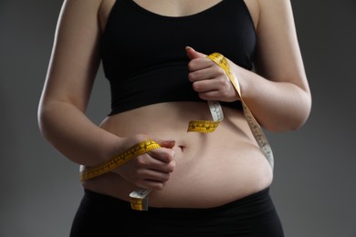 Photo of Woman measuring belly with tape on grey background, closeup. Overweight problem