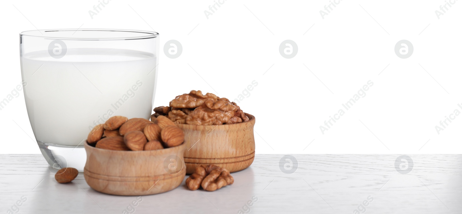 Photo of Milk in glass and nuts on table against white background