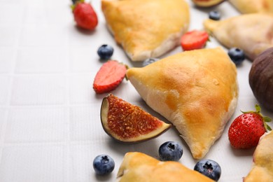 Delicious samosas, berries and fig on white tiled table, closeup