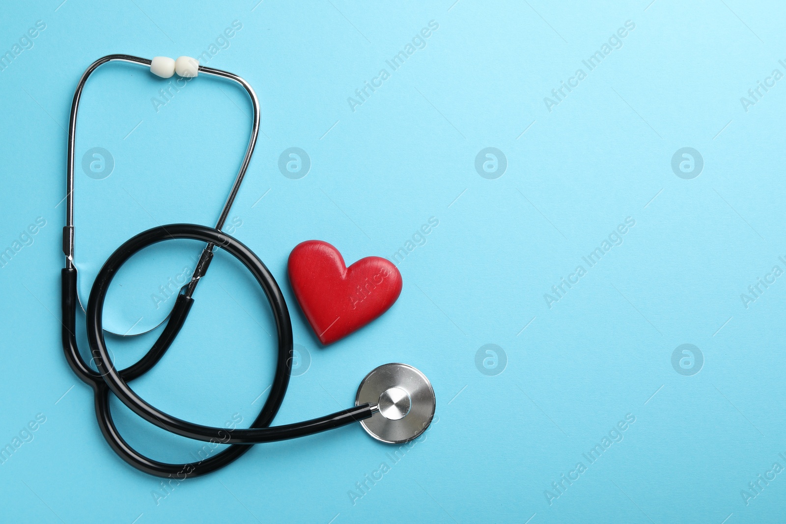 Photo of Stethoscope and red heart on light blue background, top view. Space for text