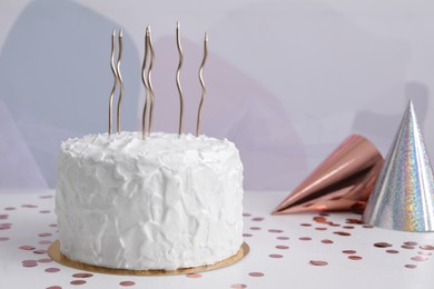 Delicious cake with candles and party hats on white table