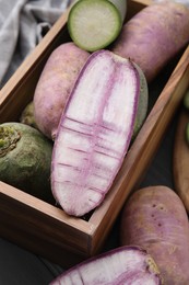Photo of Purple and green daikon radishes in crate on black wooden table, closeup