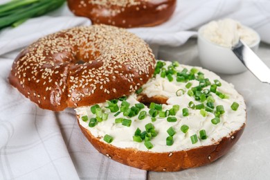 Photo of Delicious bagel with cream cheese and green onion on light table, closeup