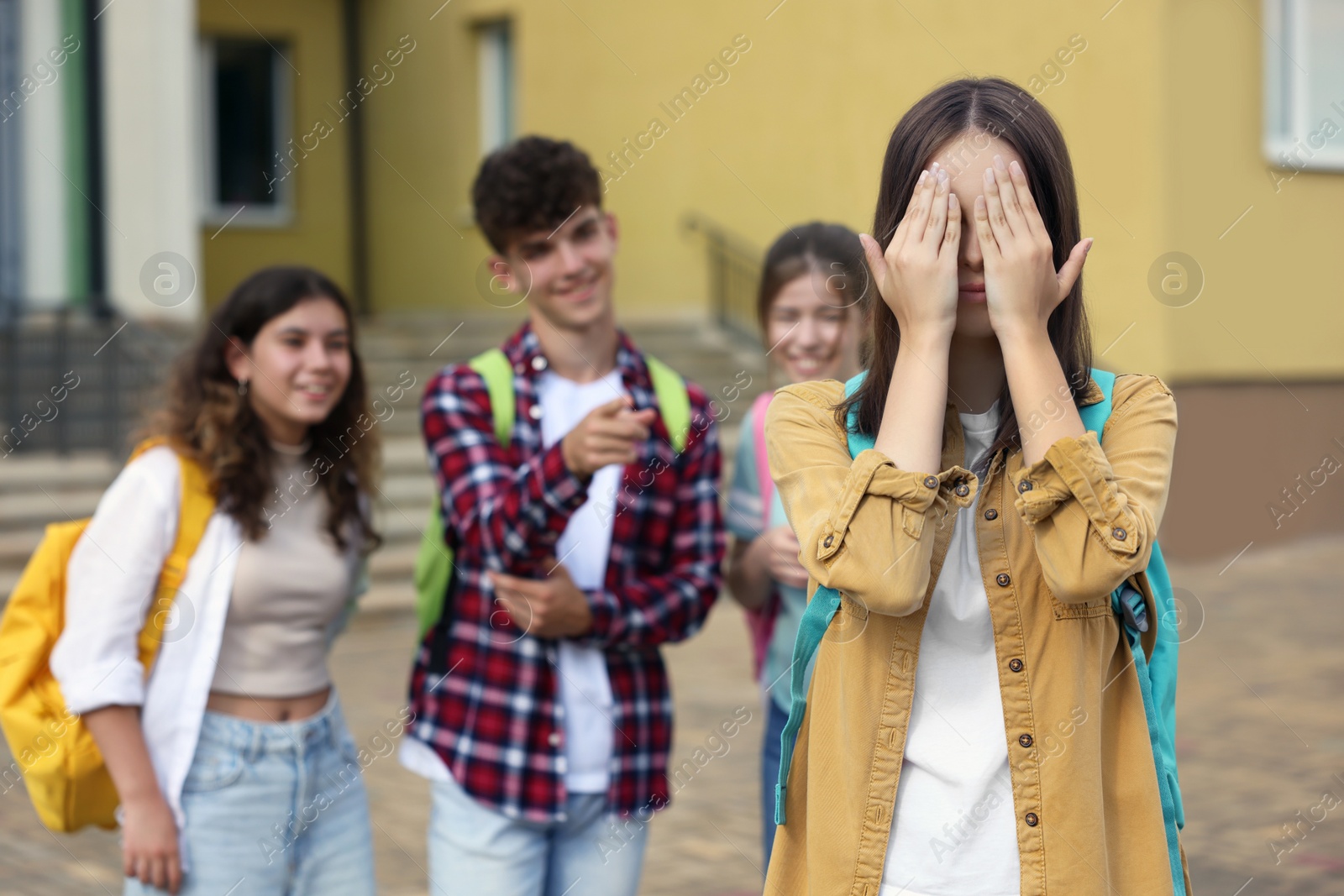 Photo of Teen problems. Lonely girl standing separately from other students outdoors