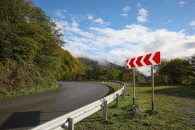 Picturesque view of empty road near trees with sign Chevron Left in mountains