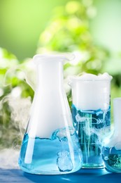 Laboratory glassware with colorful liquids on blue wooden table outdoors. Chemical reaction