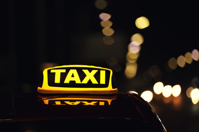 Photo of Taxi car with yellow roof sign on city street at night, closeup