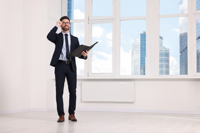 Handsome real estate agent with documents in empty room, space for text