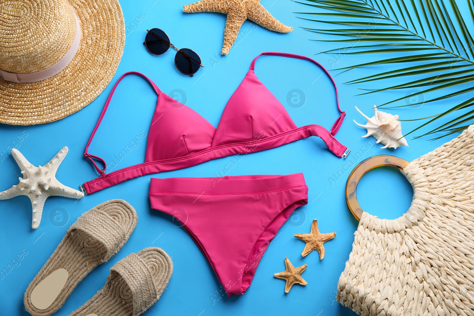 Photo of Beautiful pink bikini and beach accessories on light blue background, flat lay