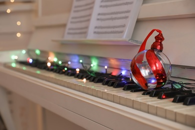 Beautiful bauble on piano keys indoors, space for text. Christmas music