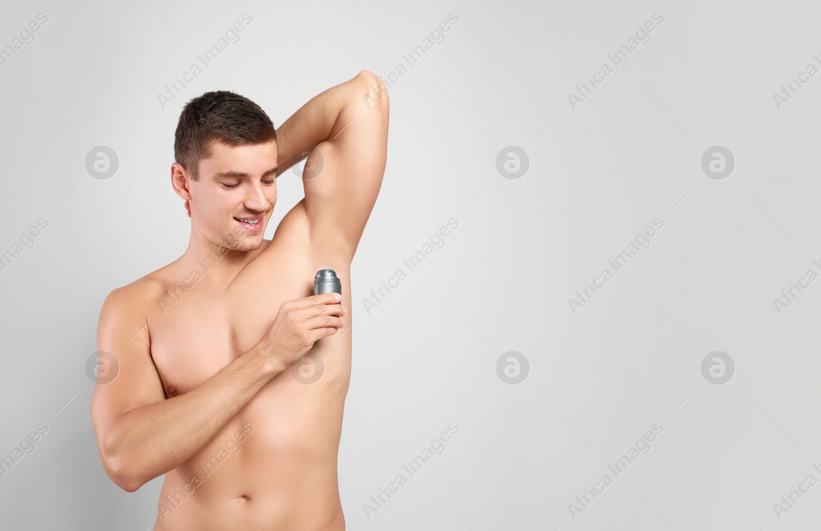 Photo of Young man applying deodorant to armpit on light background. Space for text