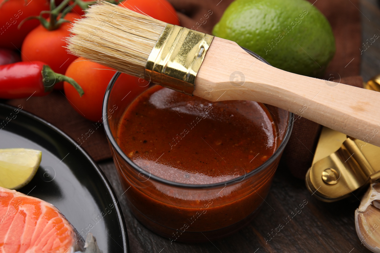 Photo of Tasty fish marinade, basting brush and products on wooden table, closeup