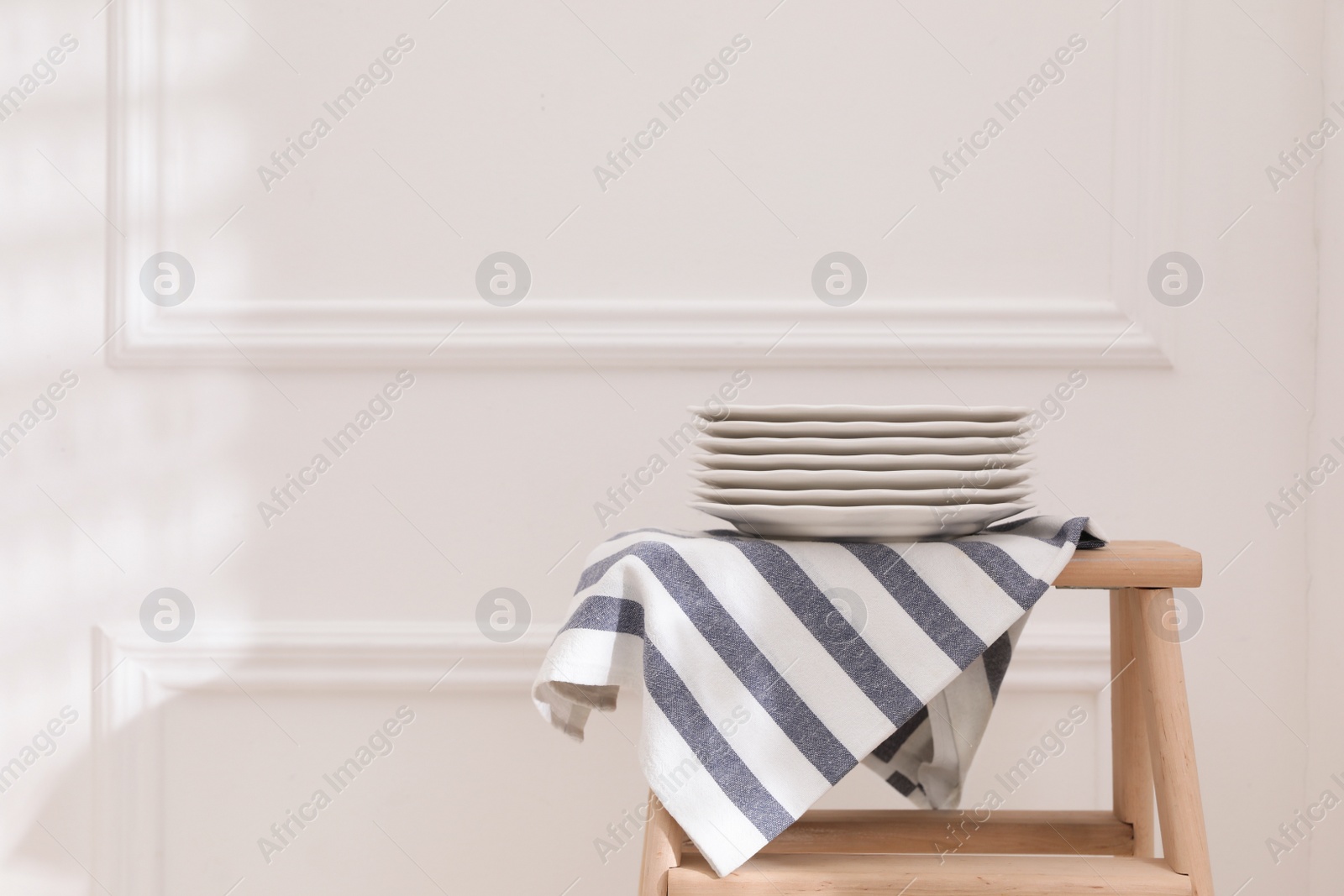 Photo of Kitchen towel and clean dishware on wooden stand near white wall. Space for text