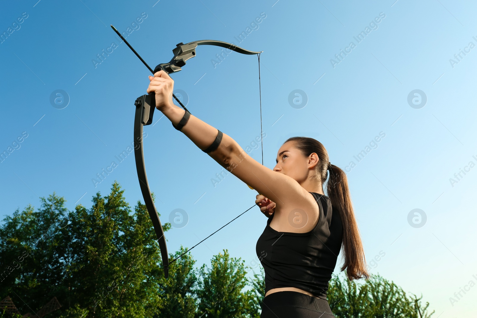 Photo of Woman with bow and arrow practicing archery outdoors, low angle view