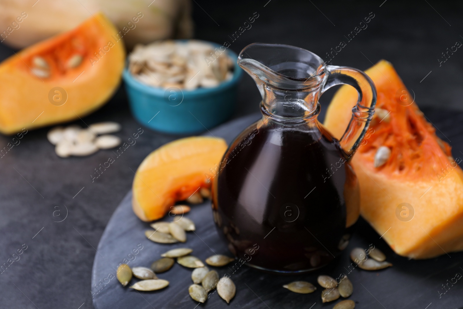 Photo of Fresh pumpkin seed oil in glass jug on dark grey table. Space for text