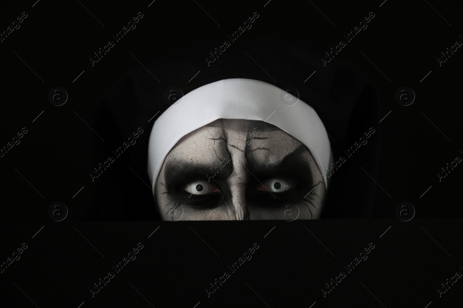 Photo of Scary devilish nun hiding on black background, closeup. Halloween party look